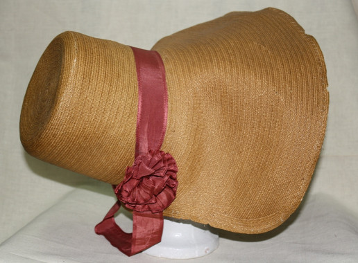 Bonnet de paille fait à la main avec des rubans de satin rose, vers 1798.
La texture de la paille qui imite le tissu était obtenue en divisant de la paille en onze brindilles.  Ces brindilles étaient par la suite tressées ensemble au moyen d'une aiguille et du fil.  (Collections de la Société d'histoire de Missisquoi)