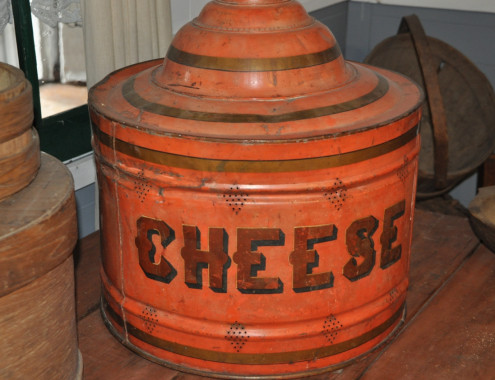Tin cheese protector, c.1890.
Cheese making was a laborious process carried out mainly by women in the household. Milk was heated on the stove and then poured into warm pans. Rennet was added to coagulate the milk to curds and whey. When the curds reached the right consistency, the whey was drained and the curds were mixed with salt. The salted curd was then placed into a cheese press to remove the remaining whey and to create a cheese. After a day in the press the cheese was allowed to age or rest in barr