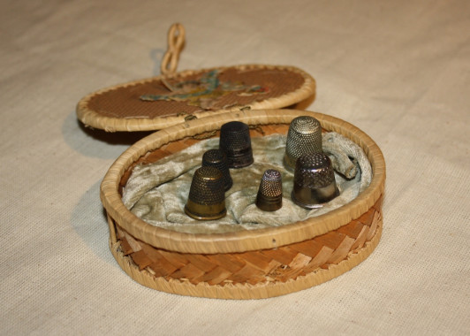 Basket of thimbles, c.1870.
Thimbles are considered one of the oldest sewing accessories still in common use today. Their basic shape has not changed in over 2,000 years and they have been found in archaeological sites including the ruins of Pompeii. In 19th century sewing boxes, thimbles often had their own special place within the box. There were even individual boxes made to exclusively hold thimbles in interesting shapes such as fruit, tiny baskets and eggs and, generally, all were lined in velvet.
(M