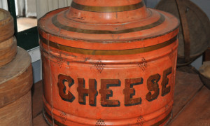 Tin cheese protector, c.1890.
Cheese making was a laborious process carried out mainly by women in the household. Milk was heated on the stove and then poured into warm pans. Rennet was added to coagulate the milk to curds and whey. When the curds reached the right consistency, the whey was drained and the curds were mixed with salt. The salted curd was then placed into a cheese press to remove the remaining whey and to create a cheese. After a day in the press the cheese was allowed to age or rest in barr