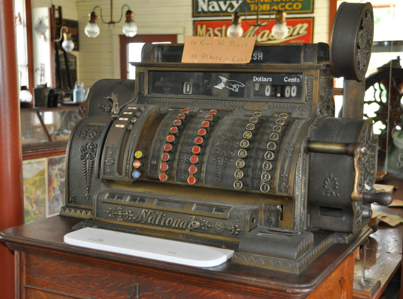 Cash register, Hodge's Store. 
The hand-written sign on the register states: "In God we trust; in all other cash." Paying one's debt in the stores of Missisquoi Bay could be settled in a number of ways. Promissory notes were popular with the wealthier citizens but most people utilized the barter system and paid with an exchange of goods or by committing themselves to labour. Items exchanged for goods purchased were all carefully recorded and had a specific cash value. Beef and pork, milk and cheese